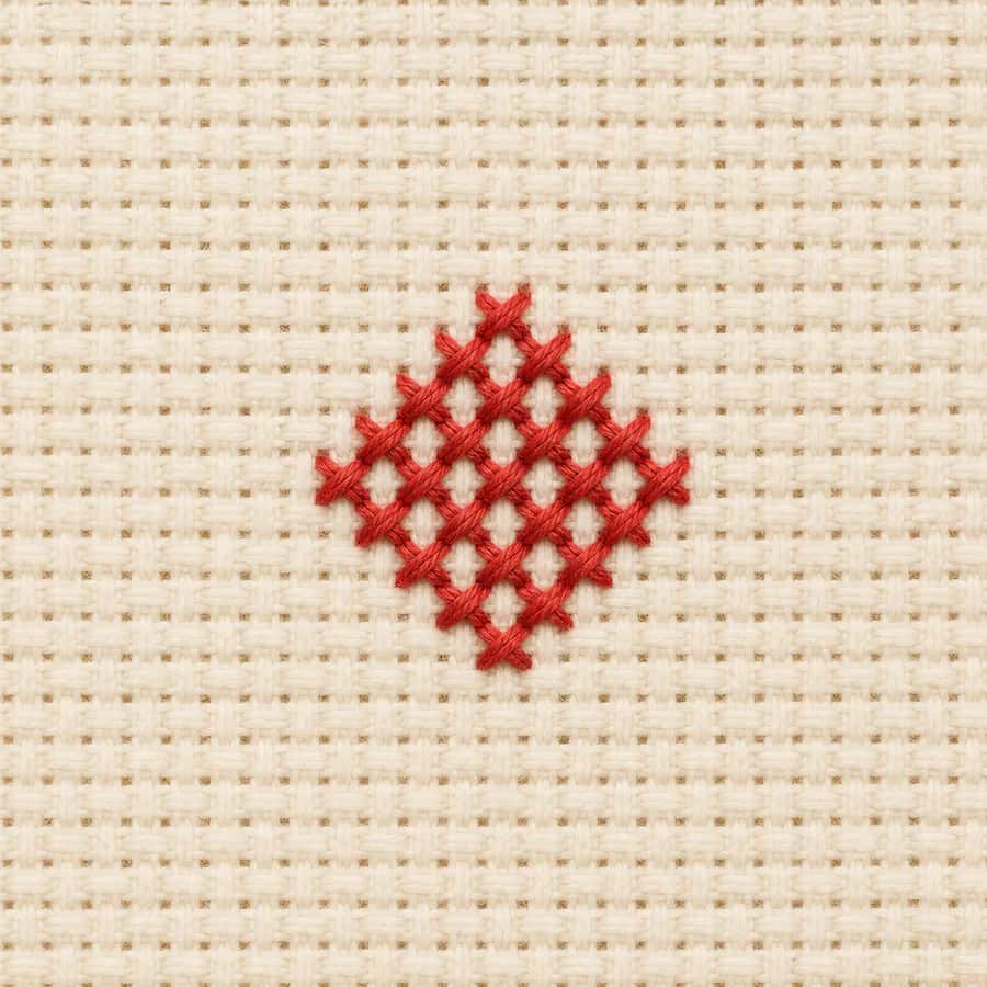 Macro view of coral full cross stitches on cream Aida cloth